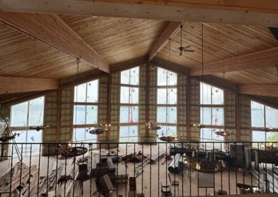 A high-angle view from a loft shows a large room with a vaulted wooden ceiling and a wall of windows undergoing major renovations