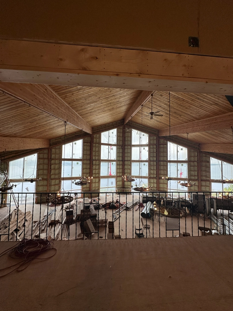 A high-angle view from a loft shows a large room with a vaulted wooden ceiling and a wall of windows undergoing major renovations